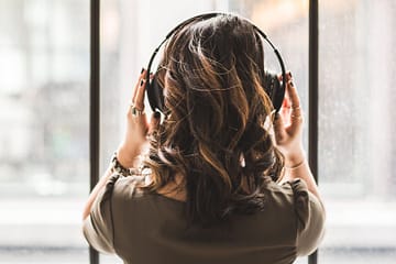 girl listening to music in front of a window wearing headphones